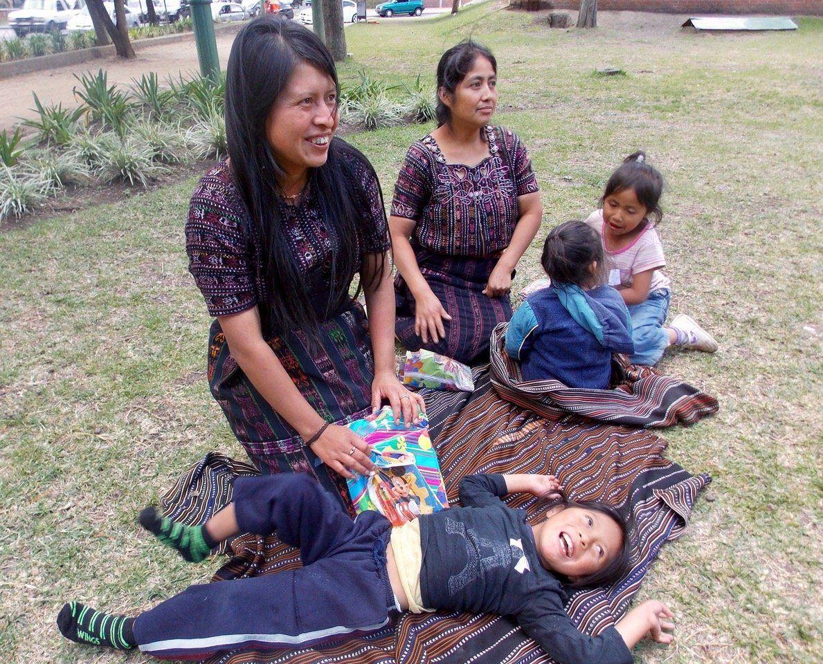 Zwei Mütter in Tracht mit Kindern auf einer Decke im Gras, ein Kind mit Behinderung lacht