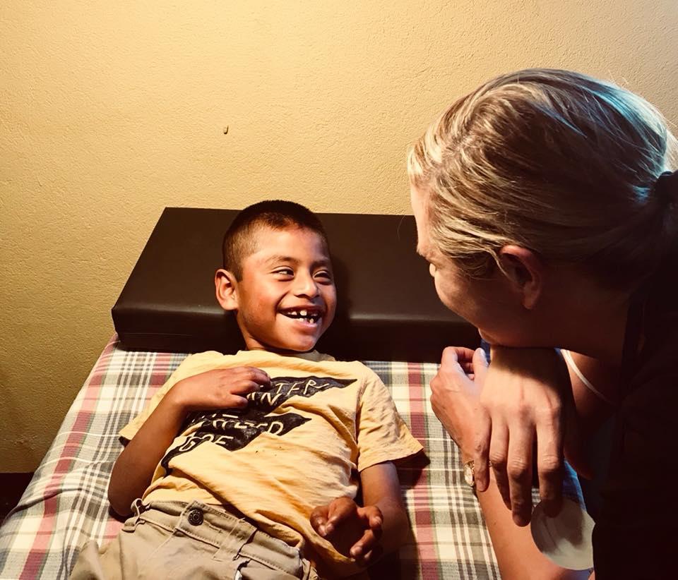 Ein lachender Junge liegt auf einer Therapieliege, eine Therapeutin beugt sich lächelnd zu ihm