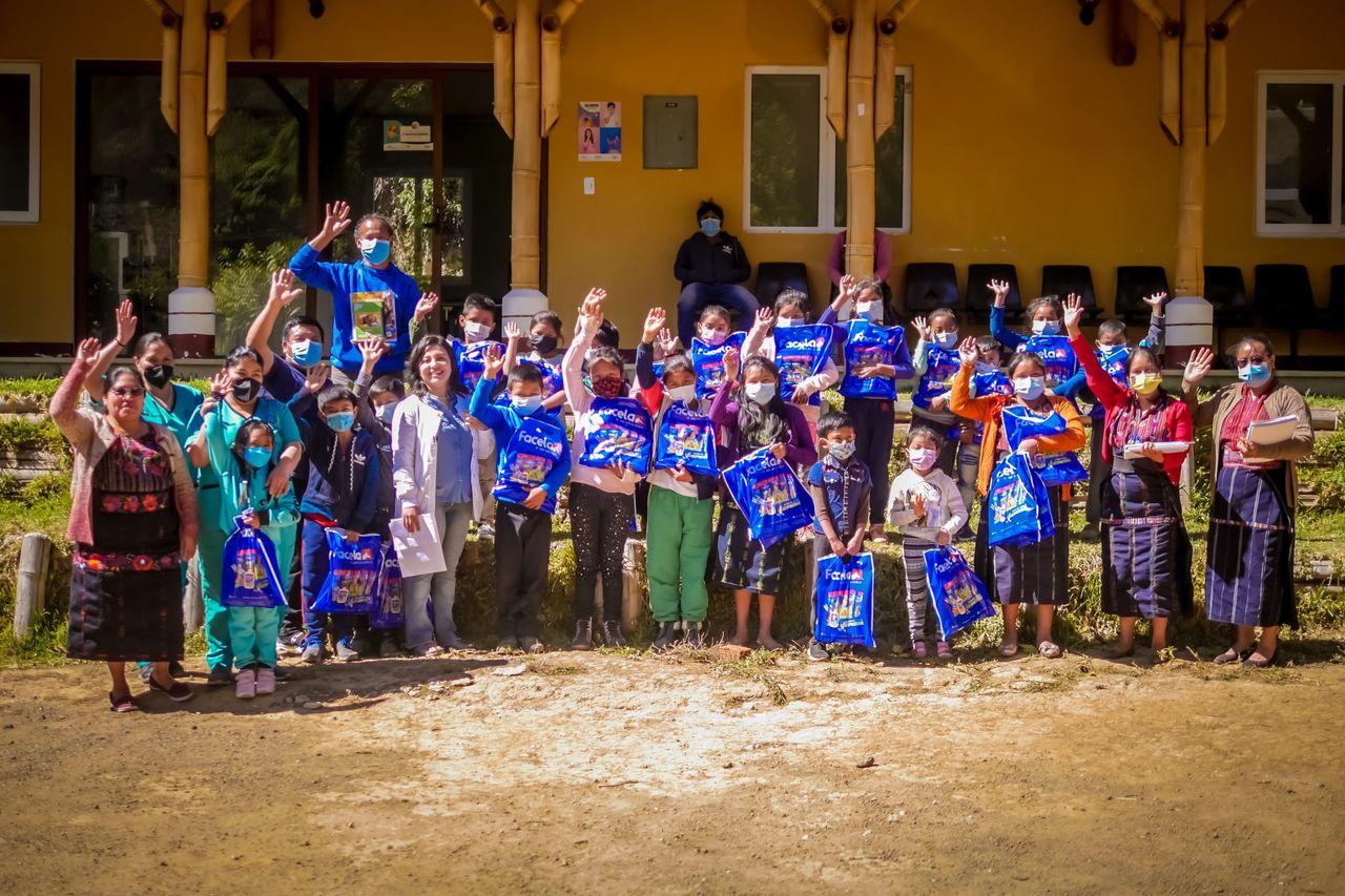 Eine große Gruppe Kinder und Mütter in Tracht vor dem Hospital, die Kinder halten neue Schulrucksäcke